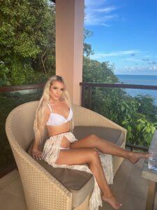 Beautiful australian blonde woman relaxing on a balcony with ocean view, wearing white lingerie
